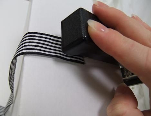 Flip the stapler open and secure the ribbon into the door Flip the stapler open and secure the ribbon into the door