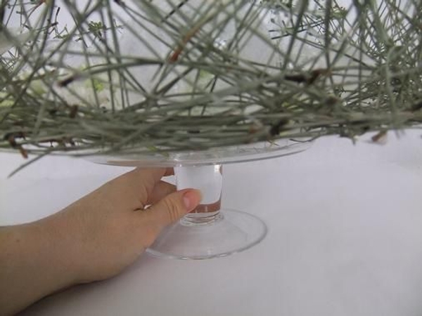 Place the Piled Pine Needle Tabletop Wreath on a glass cake stand. Place the Piled Pine Needle Tabletop Wreath on a glass cake stand.