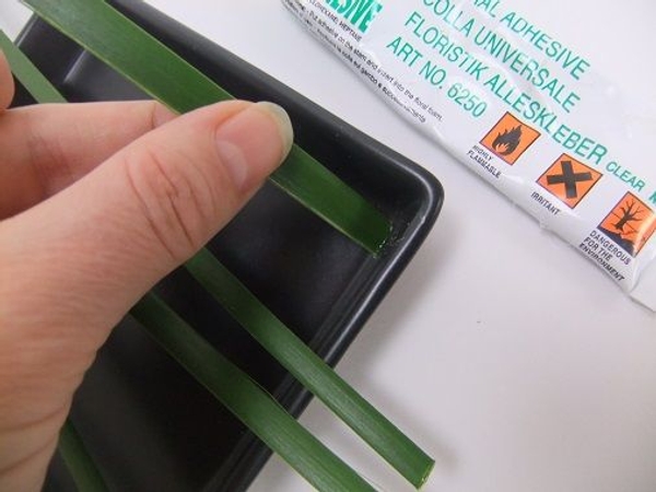 Snip a few blades of grass and glue the flat side to the side of a shallow container. Snip a few blades of grass and glue the flat side to the side of a shallow container.