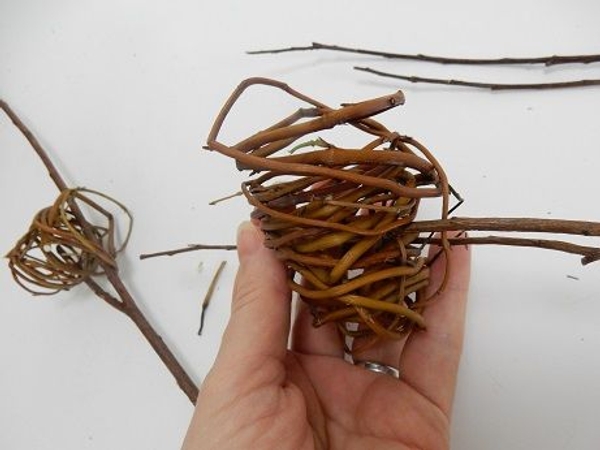 Hook the other twirled willow tube through the twig to rest in the fork Hook the other twirled willow tube through the twig to rest in the fork