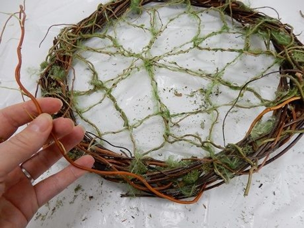 Loosely weave a few thicker stems around the armature to break up the wreath lines Loosely weave a few thicker stems around the armature to break up the wreath lines