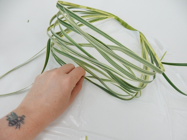 Fold the blades of grass over and secure it to the bottom of the basket, one strand at a time Fold the blades of grass over and secure it to the bottom of the basket, one strand at a time
