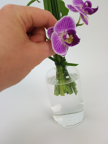 Feed the orchid stem through the grass so that it is in the water Feed the orchid stem through the grass so that it is in the water