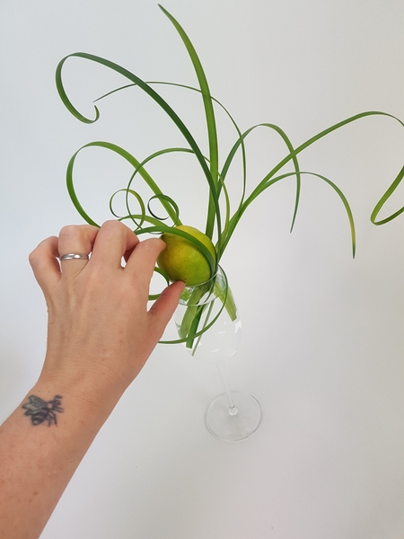 As you build up the design set the lemon at a slight angle so that the plant material are kept in place but not squished between the glass and lemon. As you build up the design set the lemon at a slight angle so that the plant material are kept in place but not squished between the glass and lemon.