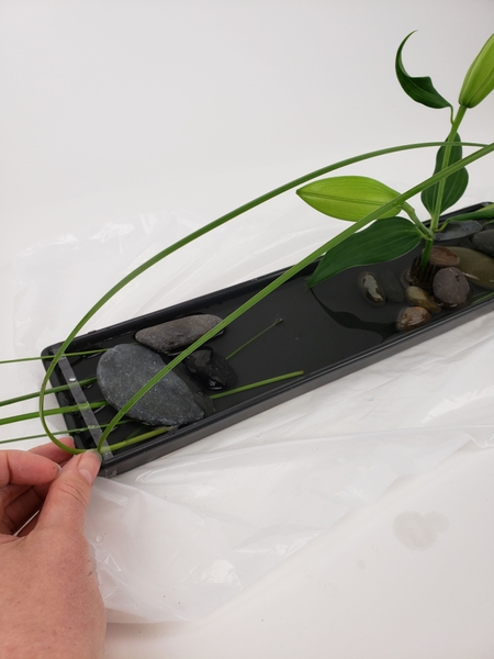 Slip the grass ends behind the tape and under the rock to keep it in place Slip the grass ends behind the tape and under the rock to keep it in place