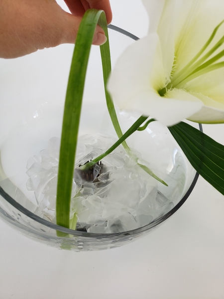 Loop the grass over the container and slip it under the pebbles on the opposite side