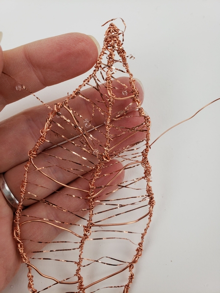 Weave the beaded wire in and around the copper wire leaf Weave the beaded wire in and around the copper wire leaf