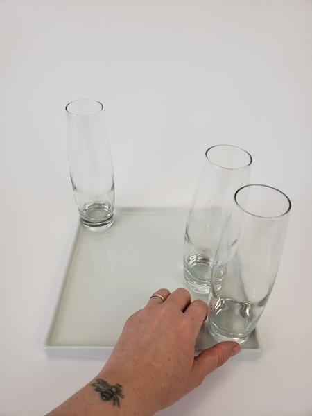 Place three bud vases in a display tray Place three bud vases in a display tray