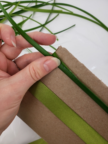 Wrap the grass strand around the cardboard in the same direction as the ribbon. Wrap the grass strand around the cardboard in the same direction as the ribbon.