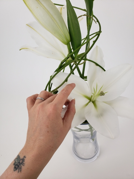 Tuck in another lily low into the vase at the back Tuck in another lily low into the vase at the back